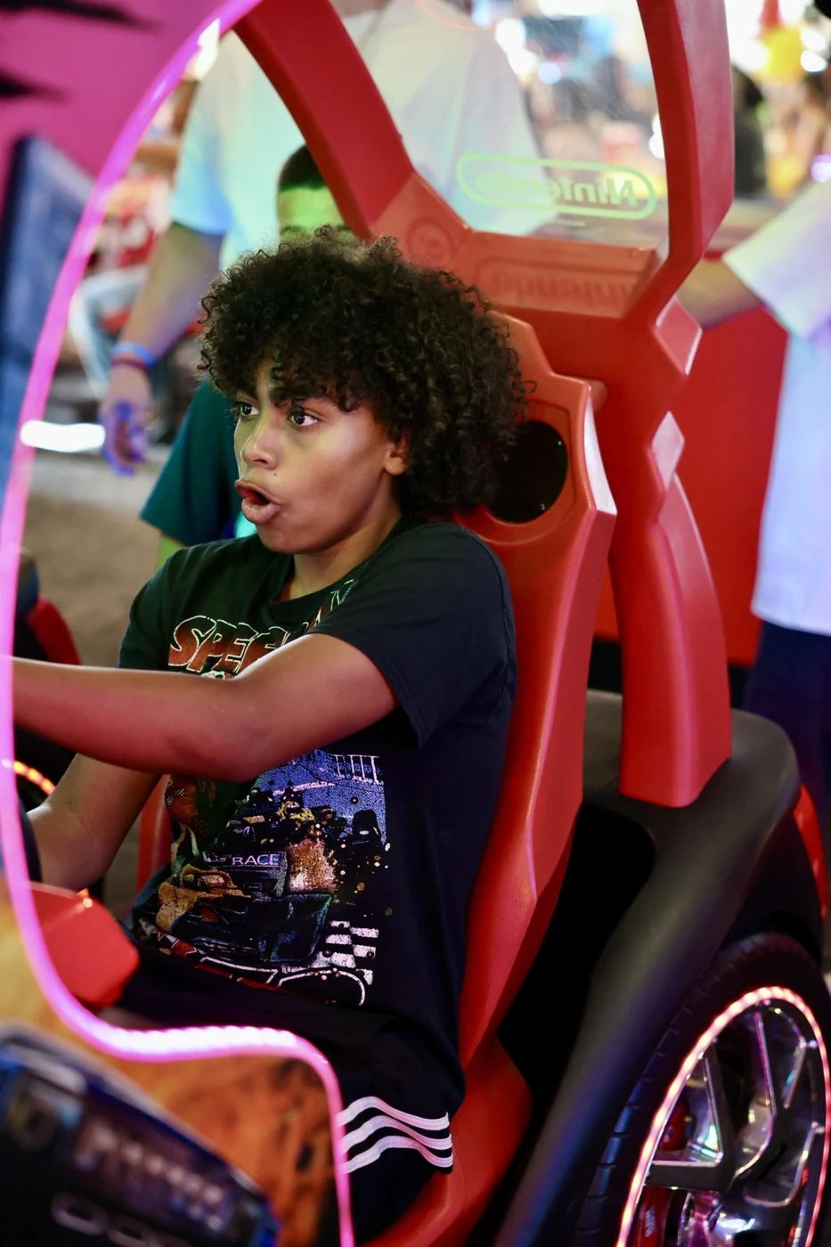 A young racer wide-eyed at the wheel of an arcade driving game